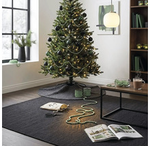 Festlich geschmückter Weihnachtsbaum mit dunklen Kugeln und Perlengirlanden in einem modern eingerichteten Wohnzimmer mit Teppich und Beistelltisch.