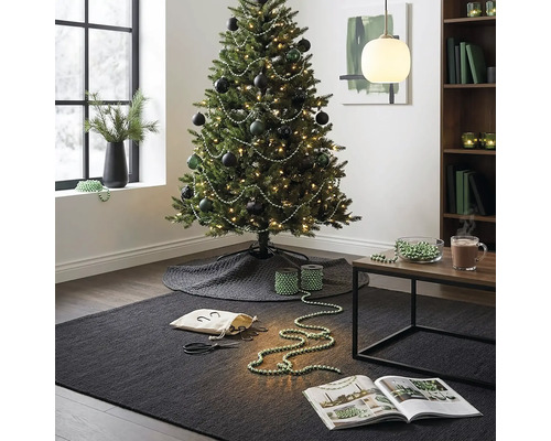 Festlich geschmückter Weihnachtsbaum mit dunklen Kugeln und Perlengirlanden in einem modern eingerichteten Wohnzimmer mit Teppich und Beistelltisch.