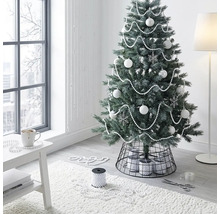 Künstlicher Weihnachtsbaum dekoriert mit weißen Kugeln und Perlenketten in einem hellen, modernen Raum mit schwarzem Metall-Christbaumständer.