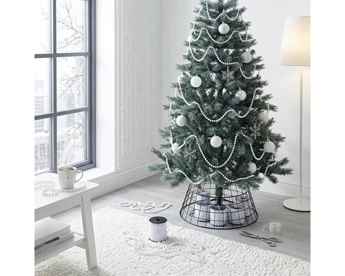 Künstlicher Weihnachtsbaum dekoriert mit weißen Kugeln und Perlenketten in einem hellen, modernen Raum mit schwarzem Metall-Christbaumständer.
