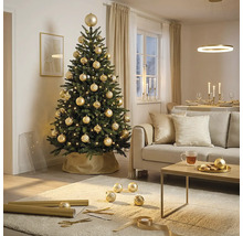 Festlich geschmückter künstlicher Christbaum mit goldenen Kugeln und Lichtern in einem hellen Wohnzimmer mit Sofa und Couchtisch.
