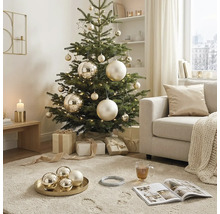 Dekorierter Weihnachtsbaum in einem hellen Wohnzimmer mit goldenen Kugeln und Geschenken.