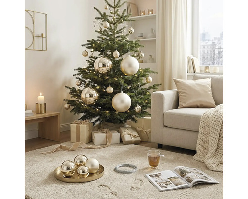Dekorierter Weihnachtsbaum in einem hellen Wohnzimmer mit goldenen Kugeln und Geschenken.