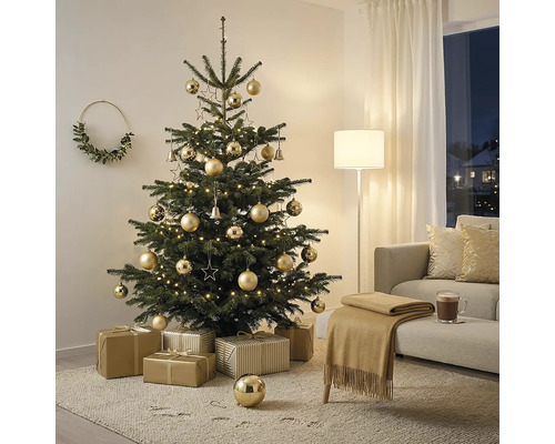 Festlich dekorierter Weihnachtsbaum mit goldfarbenem Schmuck und warmweißer Beleuchtung in einem hellen Wohnzimmer mit Sofa und Geschenken.