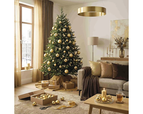 Festlich geschmückter Weihnachtsbaum mit goldenen Kugeln in einem hellen Wohnzimmer mit Sofa, Couchtisch und Weihnachtsdekoration.