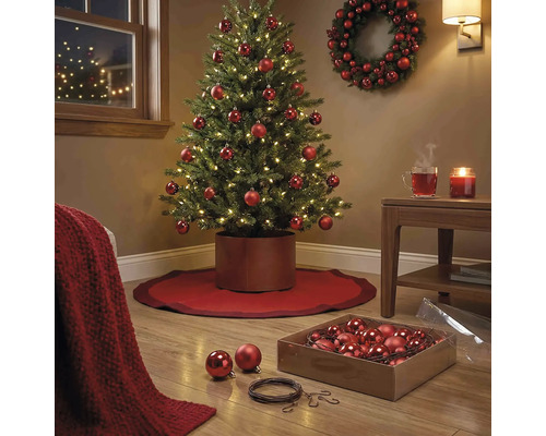 Festlich geschmückter künstlicher Weihnachtsbaum mit roten Kugeln und LED-Beleuchtung in einem wohnlichen Raum mit Kranz und Baumständer.