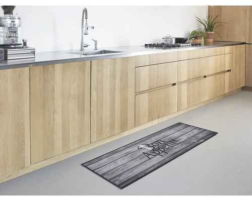 Moderne Küche mit hellen Holzelementen und einem Küchenläufer in Holzoptik mit der Aufschrift Bon Appetit auf dem hellen Fußboden.