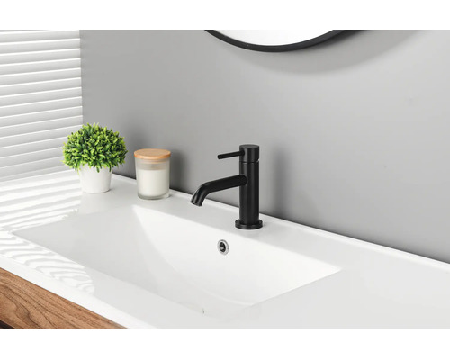 Moderne schwarze Waschtischarmatur auf einem weißen Waschbecken in einem hellen Badezimmer mit Pflanze und Kerze.