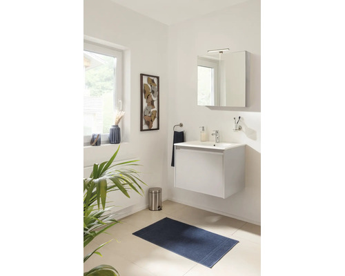 Modernes, helles Badezimmer mit weißem Hängewaschbeckenunterschrank, Spiegelschrank mit Beleuchtung und dunkelblauer Badematte.