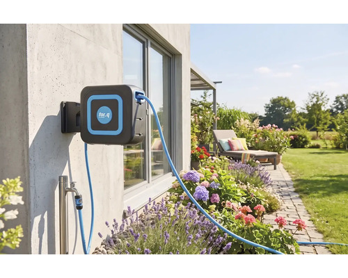 Wand-Schlauchbox von for.q an einer Betonwand, angeschlossen an einen Wasserhahn, in einem hellen, organisierten Garten mit Blumenbeeten und Rasen.