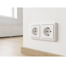 Zweifache Schutzkontakt-Steckdose horizontal montiert an einer Wand über einer Fußbodenleiste aus Holz in einem hellen, modernen Wohnraum.