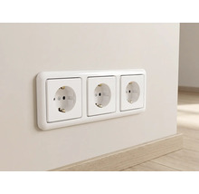 Weiße 3-fach Schutzkontakt-Steckdose mit Rahmen, waagerecht an einer Wand montiert über einer Fußleiste in Holzoptik.