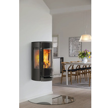 Wandhängender, schwarzer Kaminofen mit Sichtfenster und brennendem Feuer in modernem, hellen Esszimmer mit Holztisch und Glasbodenplatte.