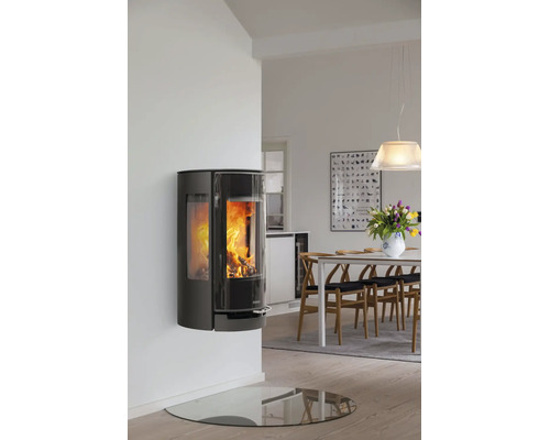 Wandhängender, schwarzer Kaminofen mit Sichtfenster und brennendem Feuer in modernem, hellen Esszimmer mit Holztisch und Glasbodenplatte.