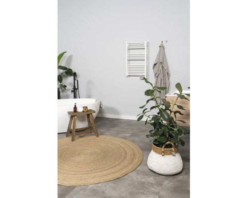 Modernes helles Badezimmer mit freistehender Badewanne, schwarzer Standarmatur, weißem Handtuchheizkörper, Holzhocker und rundem Juteteppich.