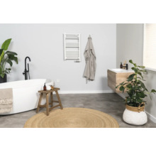 Modernes, helles Badezimmer mit freistehender Badewanne, hölzernem Waschtisch, weißem Handtuchheizkörper und rundem Jute-Teppich.
