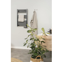 Schwarzer elektrischer Handtuchheizkörper in einem modernen Badezimmer mit Handtuch, Bademantel und Waschtisch.