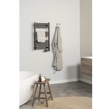 Modernes, helles Badezimmer mit einem schwarzen Handtuchheizkörper an der Wand, einer weißen Badewanne, einem Holzhocker und einem Bademantel.