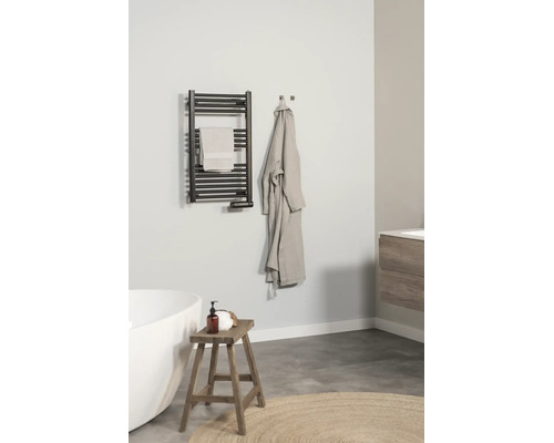 Modernes, helles Badezimmer mit einem schwarzen Handtuchheizkörper an der Wand, einer weißen Badewanne, einem Holzhocker und einem Bademantel.