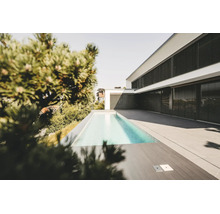 Modernes weißes Wohnhaus mit schwarzen Außenjalousien, einem schmalen Swimmingpool und einer großzügigen Terrasse mit grauen Steinplatten.