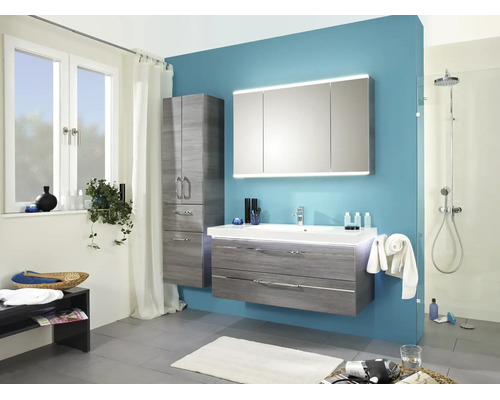 Modernes Badezimmer mit grauem Waschtischunterschrank, dreitürigem Spiegelschrank, Hochschrank und begehbarer Dusche vor blauer Wand.