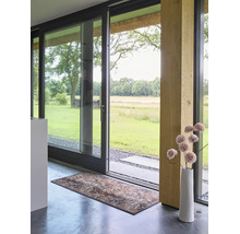 Moderner Innenraum mit großer Glasschiebetür zum Garten, dekorativem Türvorleger auf Betonboden und Holzpfeiler.