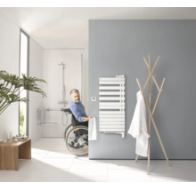 Barrierefreies Badezimmer mit Rollstuhlfahrer, Handtuchheizkörper, bodengleicher Dusche und Haltegriffen in modernem, hellem Design.