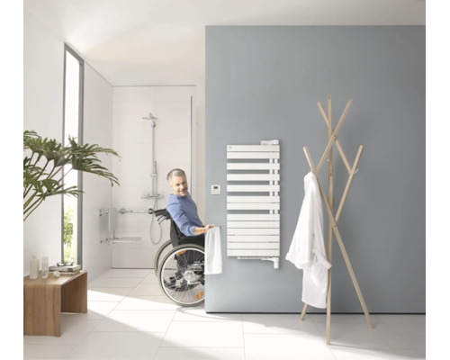 Barrierefreies Badezimmer mit Rollstuhlfahrer, Handtuchheizkörper, bodengleicher Dusche und Haltegriffen in modernem, hellem Design.