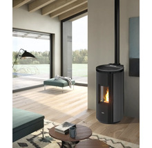 Moderner, heller Wohnraum mit schwarzem Pelletofen, sichtbarer Flamme, Holzboden, großen Fenstern mit Naturblick und petrolfarbenen Polstermöbeln.
