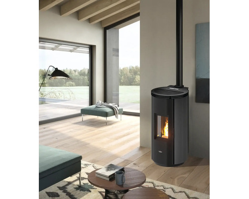Moderner, heller Wohnraum mit schwarzem Pelletofen, sichtbarer Flamme, Holzboden, großen Fenstern mit Naturblick und petrolfarbenen Polstermöbeln.