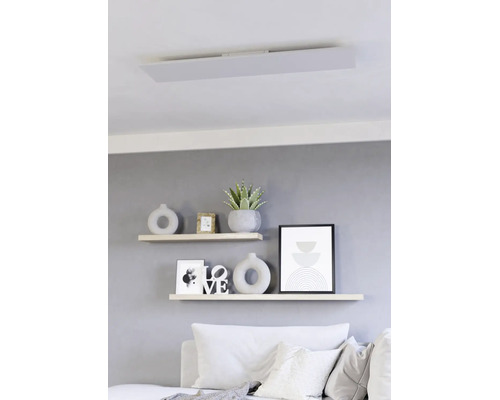 Flaches LED Panel als Deckenleuchte in einem modern eingerichteten Wohnzimmer über Wandregalen mit Dekoration.
