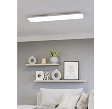 Modernes, rechteckiges LED-Panel an einer weißen Decke über einem hellen Wohnzimmer mit Wandregalen und dekorativen Elementen.