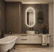 Modernes Badezimmer mit freistehender Badewanne, Unterschrank mit Riffeloptik, Aufsatzwaschbecken und ovalem LED-Spiegel vor Marmorwand.