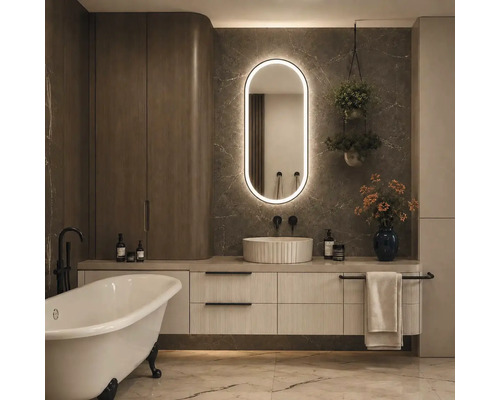 Modernes Badezimmer mit freistehender Badewanne, Unterschrank mit Riffeloptik, Aufsatzwaschbecken und ovalem LED-Spiegel vor Marmorwand.