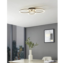 Moderne LED-Deckenleuchte mit vier überlappenden Leuchtringen in einem hellen Raum mit grauen Wänden, Tisch mit Vase und Stadtblick.
