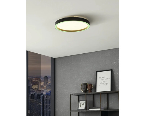 Moderne runde LED-Deckenleuchte mit schwarzem Rahmen und grünem Lichtring in einem Zimmer mit grauer Wand und Metallregal.