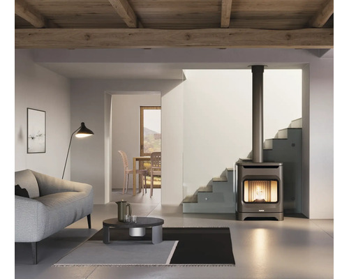 Moderner Kaminofen mit Sichtscheibe und langem Ofenrohr in einem hellen Wohnzimmer mit Sofa, Couchtisch und Holzdecke.
