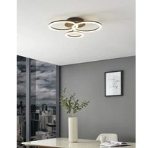 Moderne LED-Deckenleuchte mit vier leuchtenden Ringen in einem hellen Raum mit grauer Wand, Stadtblick und weißem Tisch.