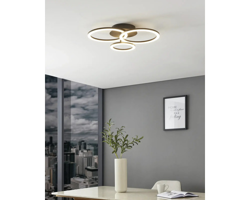 Moderne LED-Deckenleuchte mit vier leuchtenden Ringen in einem hellen Raum mit grauer Wand, Stadtblick und weißem Tisch.