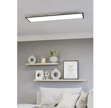 Rechteckiges LED-Panel mit schwarzem Rahmen an der Decke über einem hellen, modern gestalteten Wohnbereich mit Regalen und Sofa.
