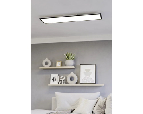 Rechteckiges LED-Panel mit schwarzem Rahmen an der Decke über einem hellen, modern gestalteten Wohnbereich mit Regalen und Sofa.