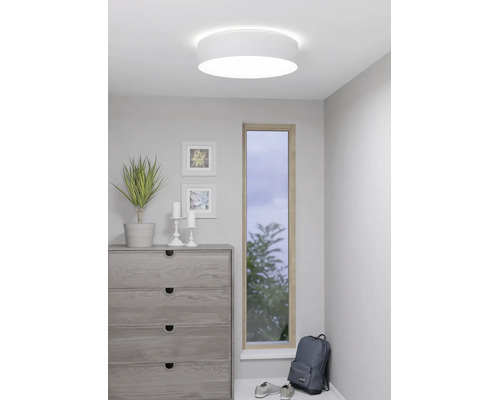 Runde weiße Deckenleuchte in einem modernen Zimmer mit einer Kommode, einer Pflanze und einem schmalen Fenster.