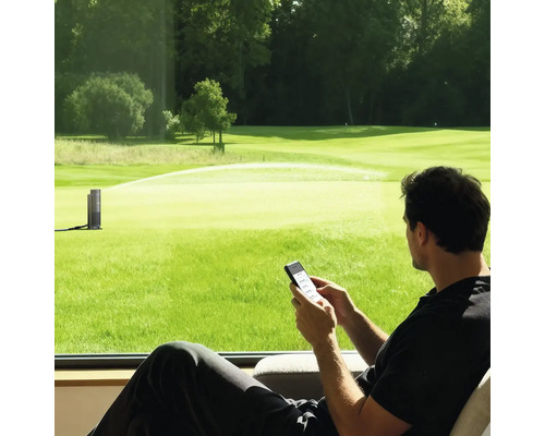 Mann steuert einen smarten Gartenregner per Smartphone-App mit Blick auf eine große Rasenfläche.