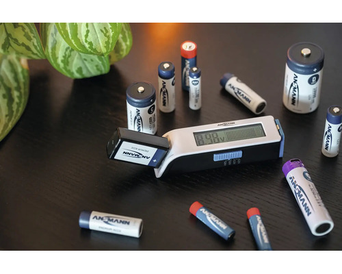 Ansmann Batterietester mit Digitalanzeige und verschiedenen Ansmann Batterien auf einem Tisch.