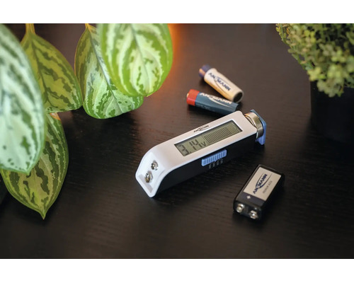 Ansmann Batterietester mit digitalem Display zur Messung von verschiedenen Batterietypen, liegend auf einer Tischoberfläche mit weiteren Batterien.