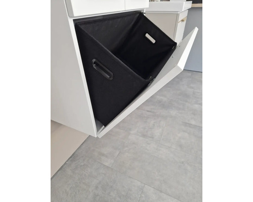 Badezimmerunterschrank mit offenem, schrägem Auszug und einem schwarzen Textilkorb.