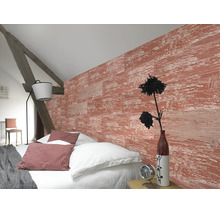Helles Schlafzimmer mit strukturierter Wand in roter Holzoptik, weißem Bettzeug, rustikalem Holzbalken und einer modernen Stehlampe.