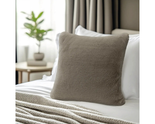 Quadratisches Dekokissen aus weichem Kunstfell in Taupe, platziert auf einem Bett mit weißer Bettwäsche.