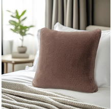 Quadratisches Dekokissen in Kunstfell-Optik auf einem Bett mit Decke und Kissen im Hintergrund.