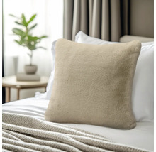 Weiches Kunstfell-Zierkissen in Beige auf einem Bett mit weißer Bettwäsche, im Hintergrund ein Beistelltisch mit Pflanze.